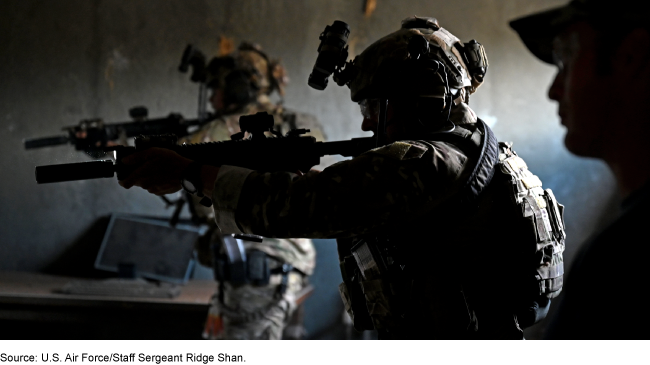 U.S. soldiers wearing tactical gear and moving through a building with cement walls