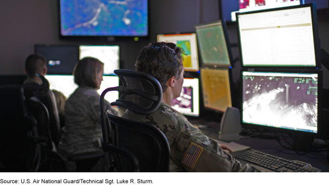 Uniformed servicemembers working at computers with multiple screens