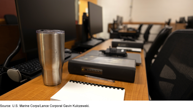 A row of empty desks and chairs with an unattended cup of coffee and binders in the foreground, with additional empty desks in the background. A row of empty desks and chairs with an unattended cup of coffee and binders in the foreground, with additional empty desks in the background.