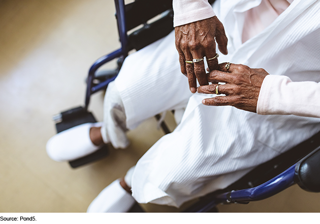 Close up view of the hands of an older person who is sitting in a wheelchair.