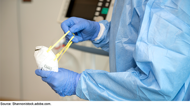 A person wearing a medical gown and gloves holding a mask