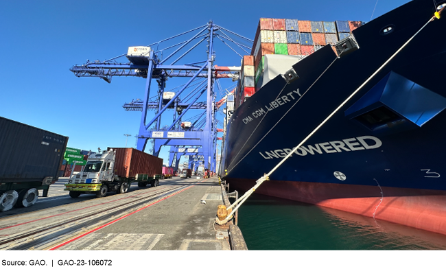 A ship tied to a dock with trucks and trains unloading shipping containers