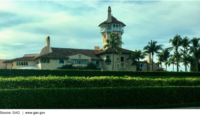 Yellow building with a tower by palm trees with a hedge in front