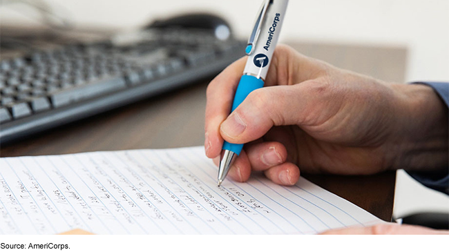 A hand writing on a notebook on a desk. 