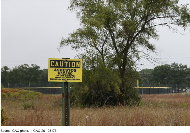 Yellow sign that says Caution, Asbestos Hazard on a grassy field. 