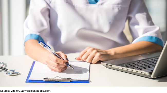 A person in scrubs taking notes with a pen on a clipboard.