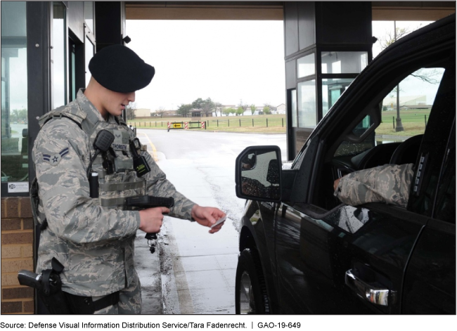 A person in a military uniform checks a car stopped at a checkpoint.