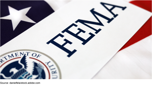 Logo for FEMA printed on a piece of paper, which is sitting on top of a very large American flag. Logo for FEMA printed on a piece of paper, which is sitting on top of a very large American flag.