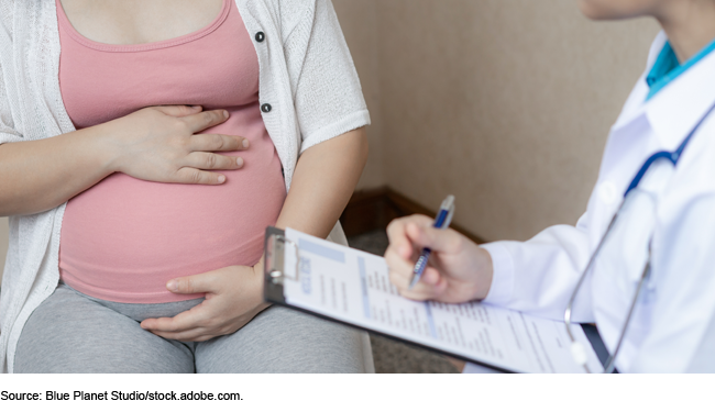 Pregnant woman with her hands on her belly sits beside a medical professional. 
