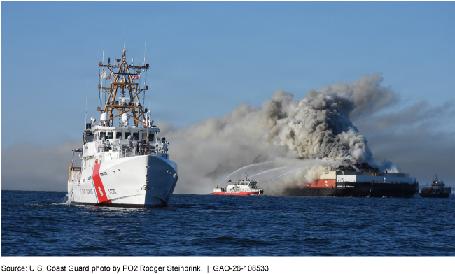 A large white ship in the foreground with a smaller boat in the background spraying water on a larger ship with smoke billowing off it. A large white ship in the foreground with a smaller boat in the background spraying water on a larger ship with smoke billowing off it.