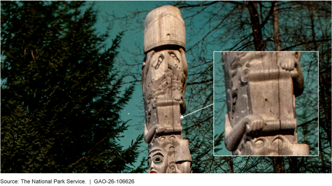 A tall pole-like structure with intricate cultural carvings in a forest. The pole shows a closeup of a figure holding a scroll.