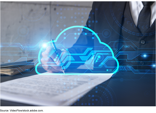 A person at a desk wearing a business suit is signing a contract. Above the contract is an image of an electronic cloud.