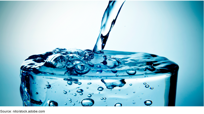 A glass with water being poured into it that is overflowing.