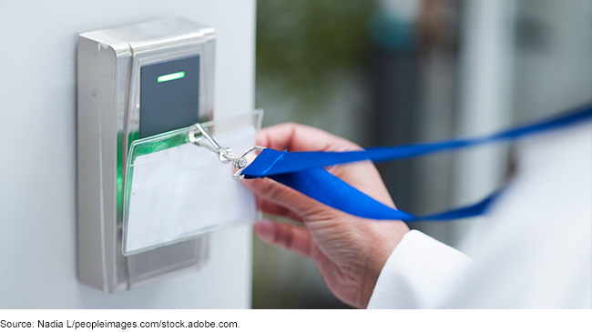 A person in a lab coat swiping a badge on a reader in a secure facility.