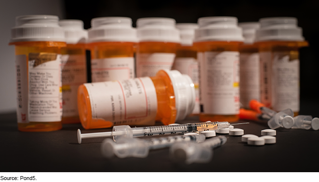 Syringes, pills and pill bottles on a black surface.