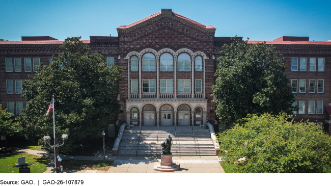 The front of a brick school building with a stairway leading up to the entrance.