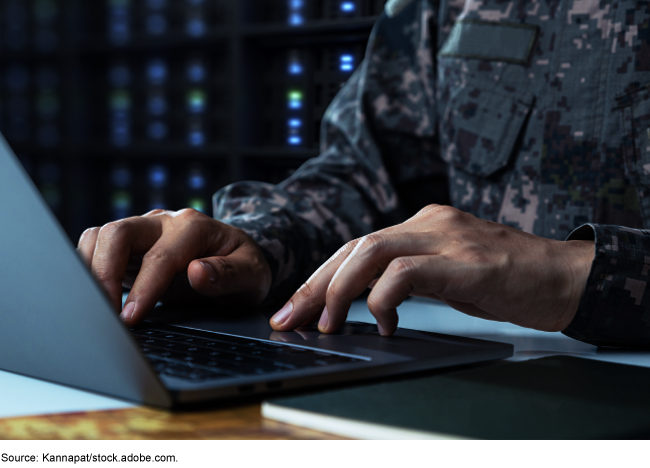 A uniformed servicemember typing on a laptop
