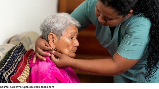 A caregiver helping an elderly patient put her earring on in an assisted living facility.
