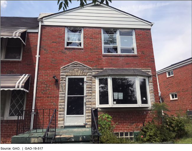 A brick rowhouse with notices in the front window and a crooked porch light