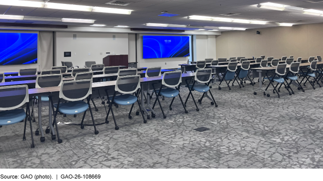 A conference room with 6 long tables and 40 chairs, arranged classroom-style facing 2 large monitors A conference room with 6 long tables and 40 chairs, arranged classroom-style facing 2 large monitors