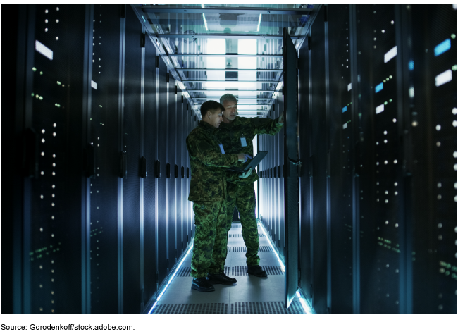 In a data center, two military men work with an open server rack cabinet. One holds a military edition laptop. In a data center, two military men work with an open server rack cabinet. One holds a military edition laptop.