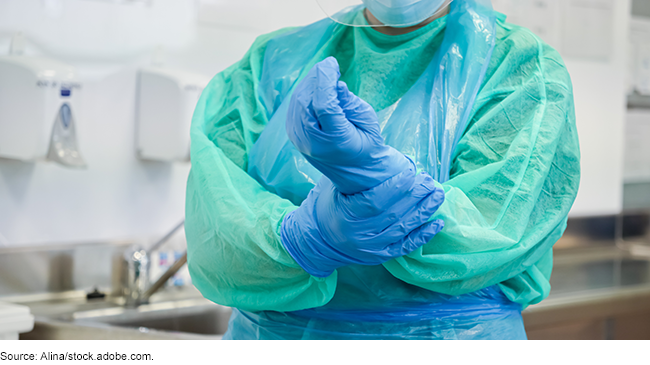 A person with medical surgery clothing on, securing the glove on their hand.