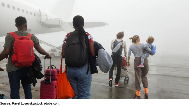 Group of people are walking on the tarmac of an airport. One of the people is carrying a baby near airplane in fog