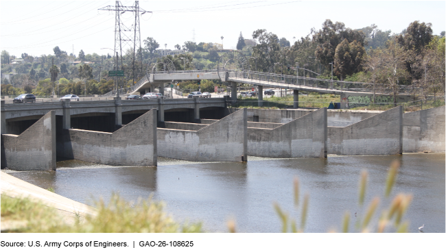 A bridge with cars on it over a river with several large concrete structures running parallel in the river. A bridge with cars on it over a river with several large concrete structures running parallel in the river.
