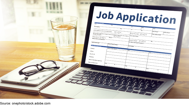 A laptop showing a job application form, notebooks, and a glass of water on a desk