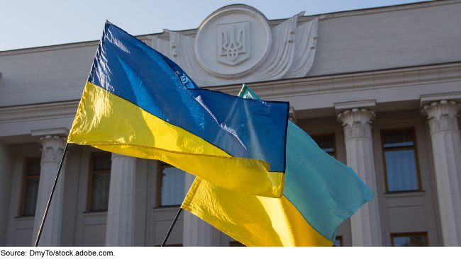 Photo showing two blue and yellow Ukrainian flags outside of a Ukrainian government building.