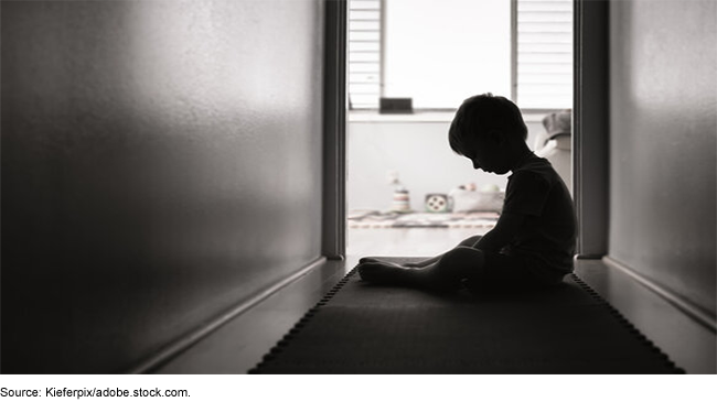 black and white photo of a young child sitting alone in a dark hallway