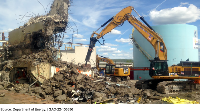 An excavator working in rubble near a partially demolished structure.