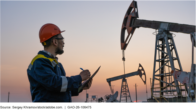An oil and gas worker checks oil pump jacks and records data on a clipboard at sunset. 