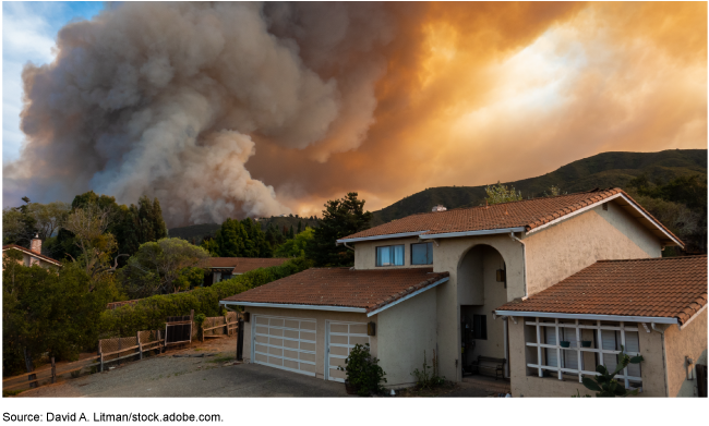 A house with a massive amount of smoke rising into the sky behind it.