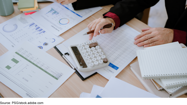 Person examining project reports and using a calculator.  