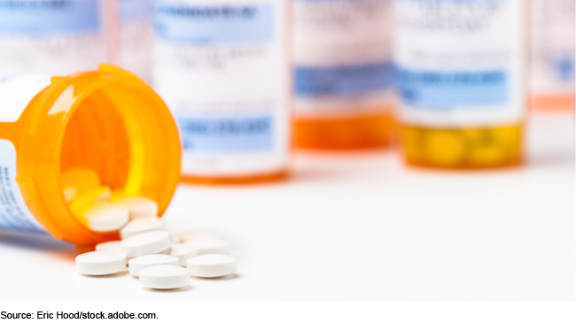 A prescription drug vial on its side with pills spilling out of it, with other upright vials in the background.