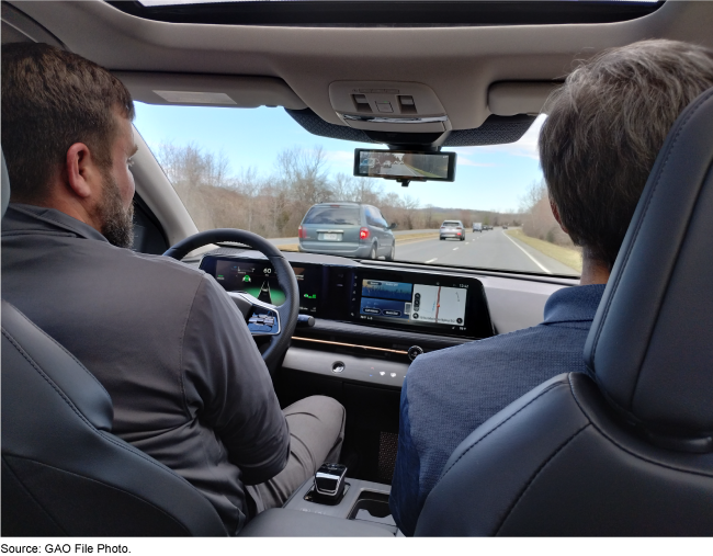 Two people inside a car using driver assisted technology on an interstate.