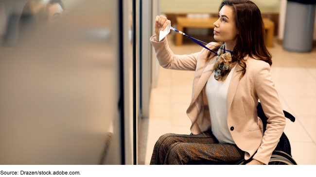 Woman, wearing dress clothes, who uses a wheelchair, scanning her badge attached to a lanyard to enter a room.