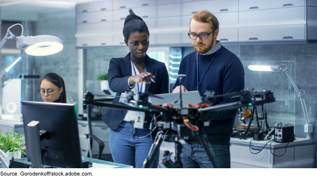 Photo showing two people standing together and looking at a drone. 