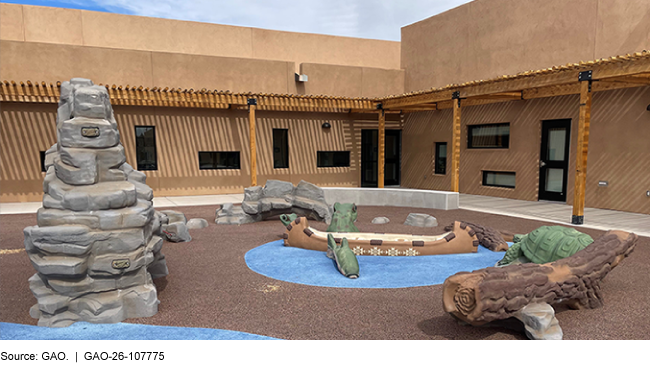 A courtyard in a pueblo-style building with playground climbing structures shaped like rocks, turtles, logs, and a canoe A courtyard in a pueblo-style building with playground climbing structures shaped like rocks, turtles, logs, and a canoe