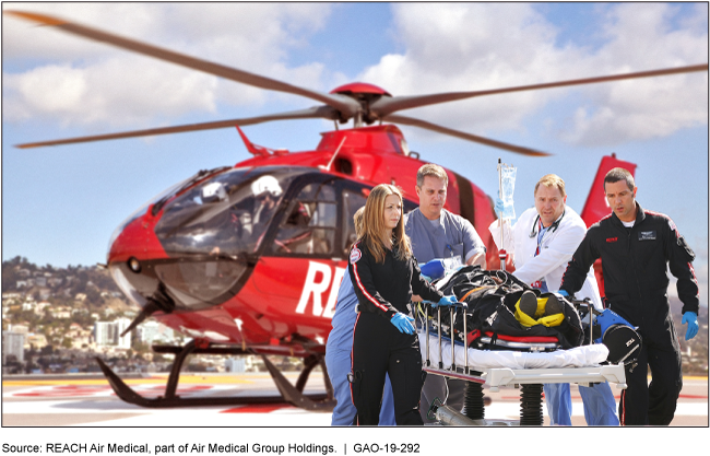 Doctors and EMTs on a helipad push a gurney with an immobilized patient away from a red helicopter