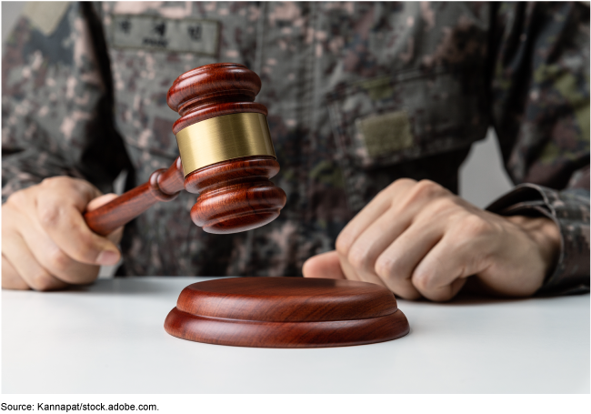 A military service member in uniform holding a judge's gavel. 