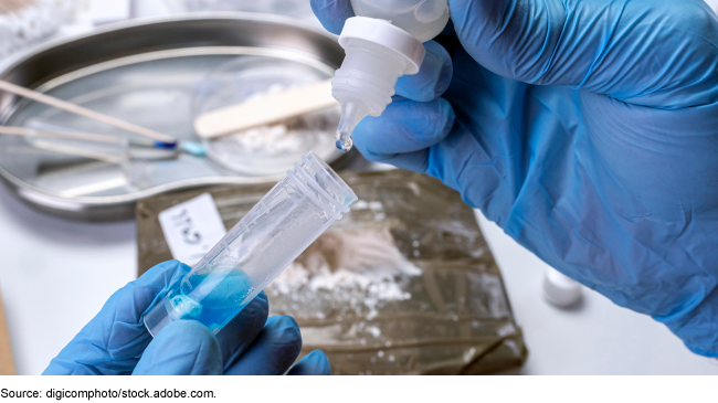 A person wearing blue medical gloves using a dropper to put a substance into a small transparent tube. 