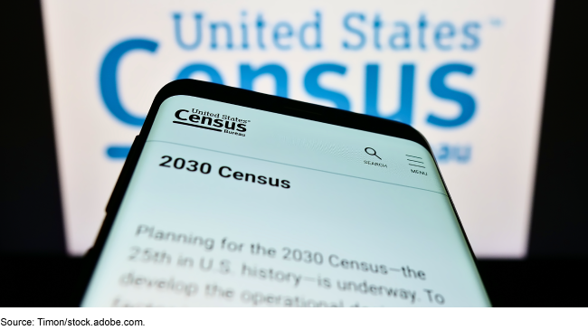 A smartphone displaying information on the 2030 Census in front of a large Census Bureau logo graphic.