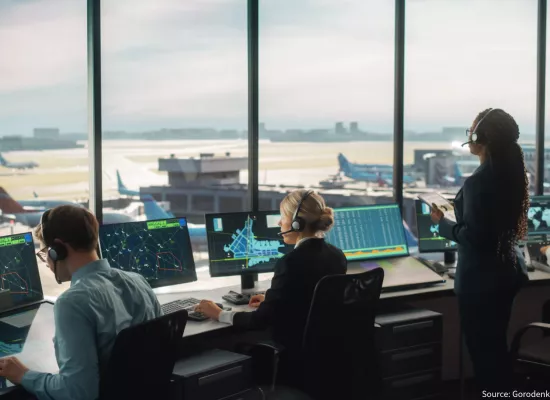 4 air traffic controllers sit in an air traffic control tower looking at screens and the runway in front of them.