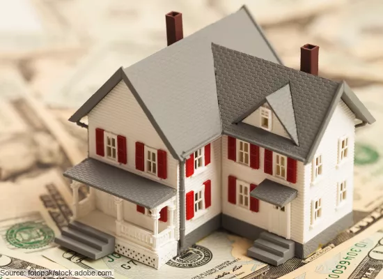 Stock image showing a toy house sitting on a pile of money.