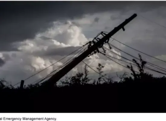 Image shows a downed powerline pole silhouetted against a stormy sky.