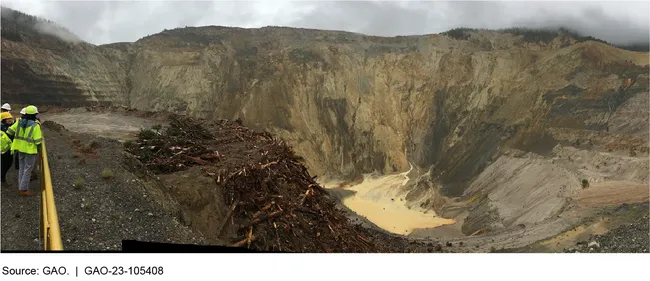 Photograph showing a large pit in the mountains with people wearing construction gear on the side.