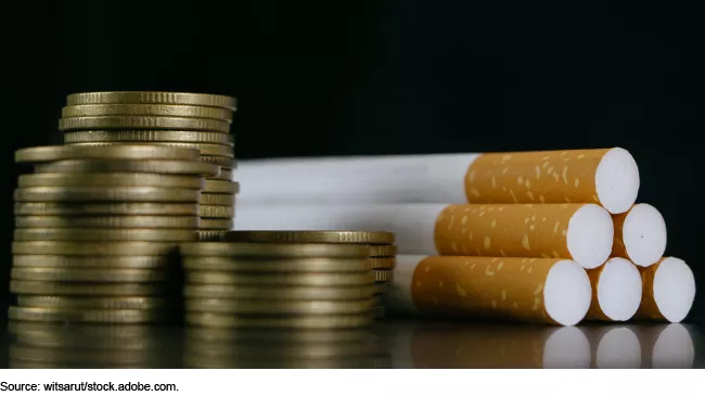 Photo showing a stack of gold coins on left with a stack of cigarettes on right.