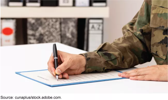 Stock image showing a person wearing military fatigues signing a loan document.